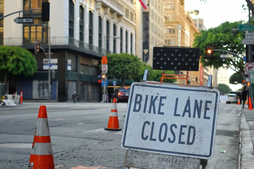 Close-up of Bike Lane Closed sign on street in downtown Los Angeles with orange traffic cones blocking lane in background.